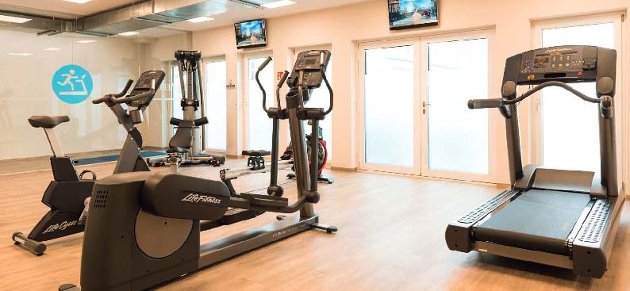 Foto des Fitnessraums mit mehreren Sportgeräten unter anderem einem Laufband.